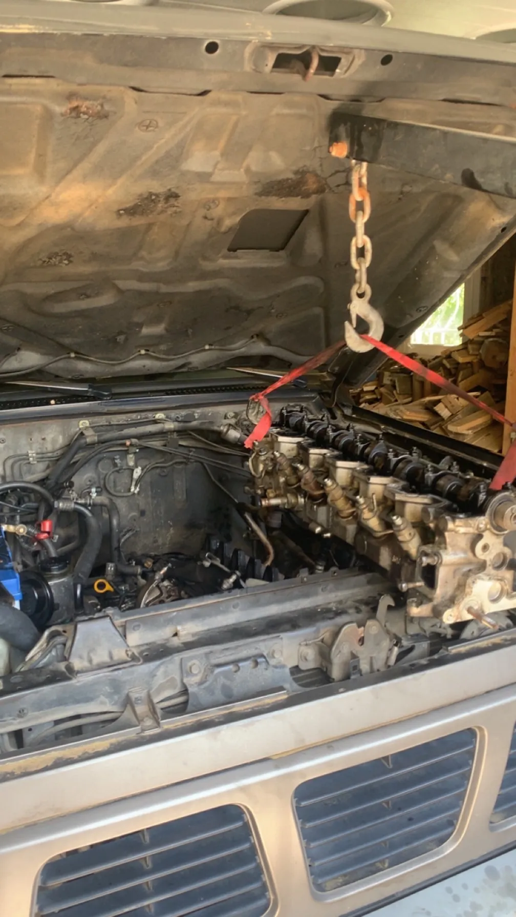 Dépose de moteur par chaîne et palan sous capot ouvert, intervention mécanique lourde en atelier.