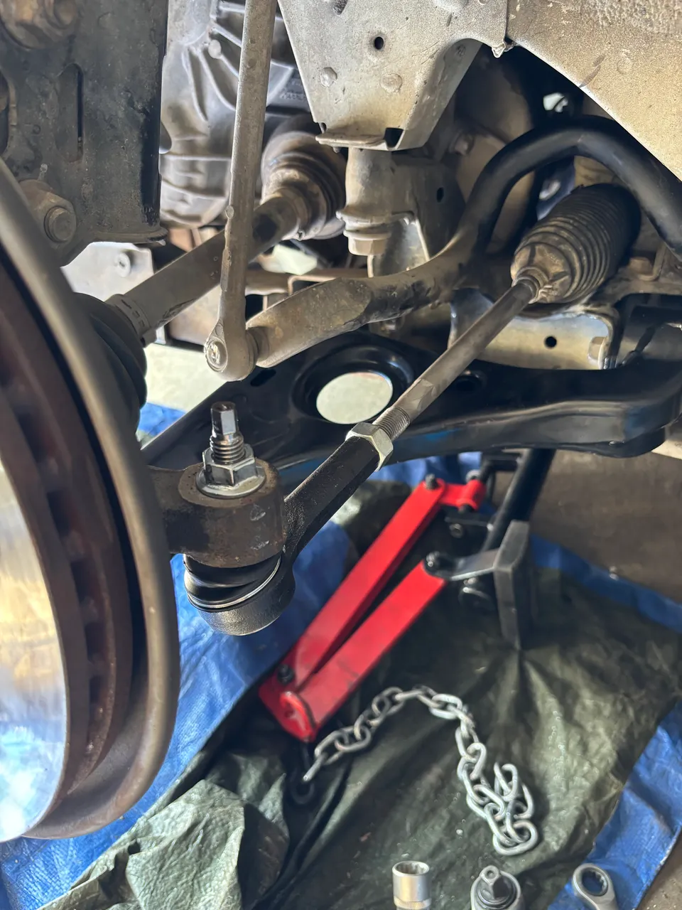 Bras de suspension et rotule de direction vus sous un véhicule en atelier, intervention mécanique sur le train avant.